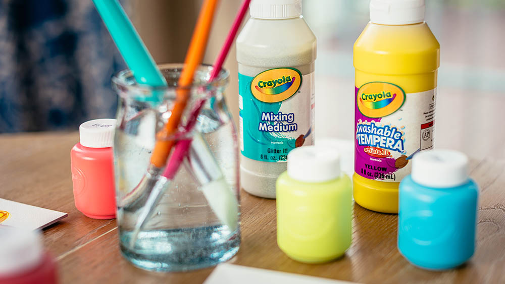 Acrylic pains and some brushes in water on a desk.